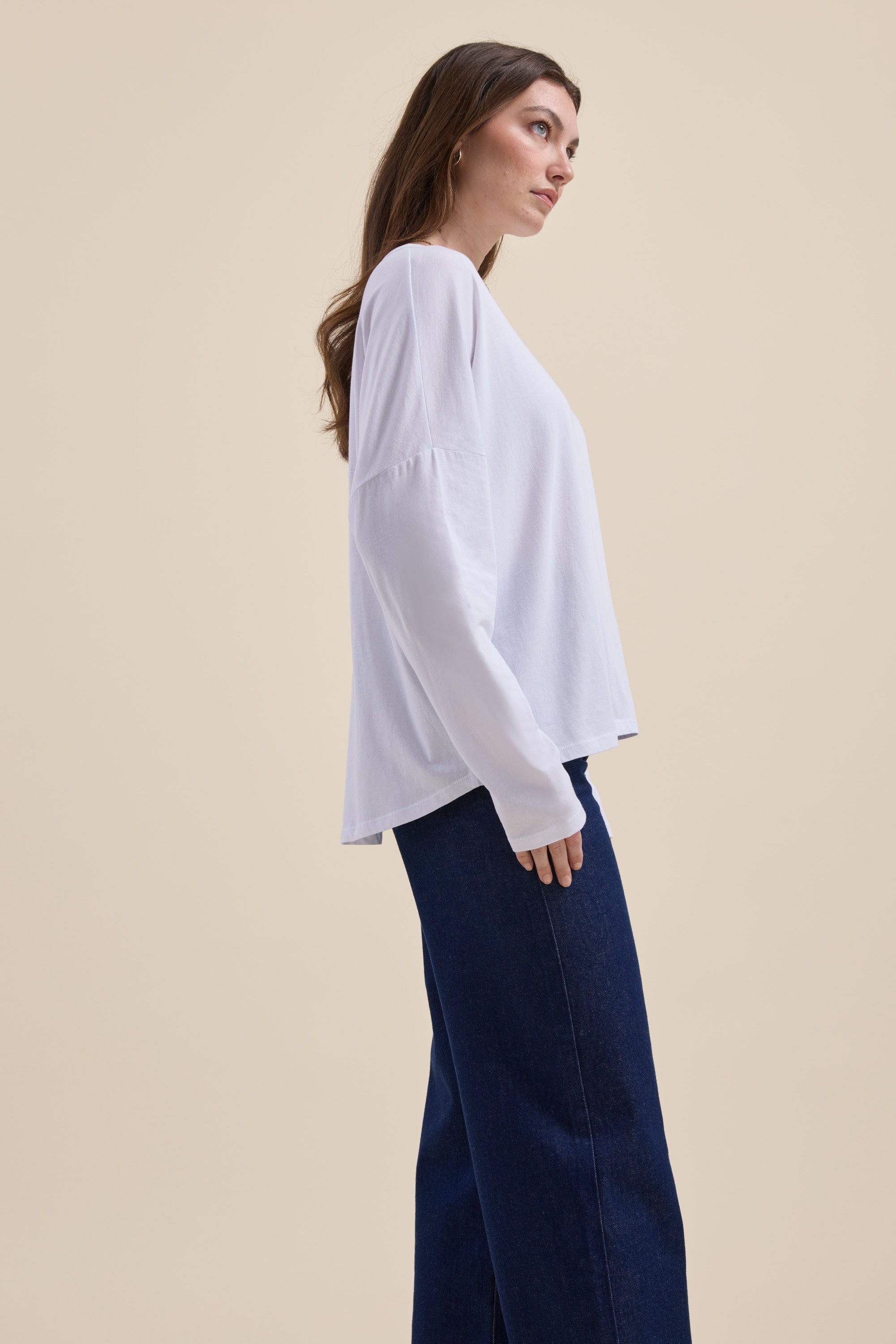 Woman in Max Elementary Slouchy Long Sleeve Tee and dark blue jeans stands by beige background.