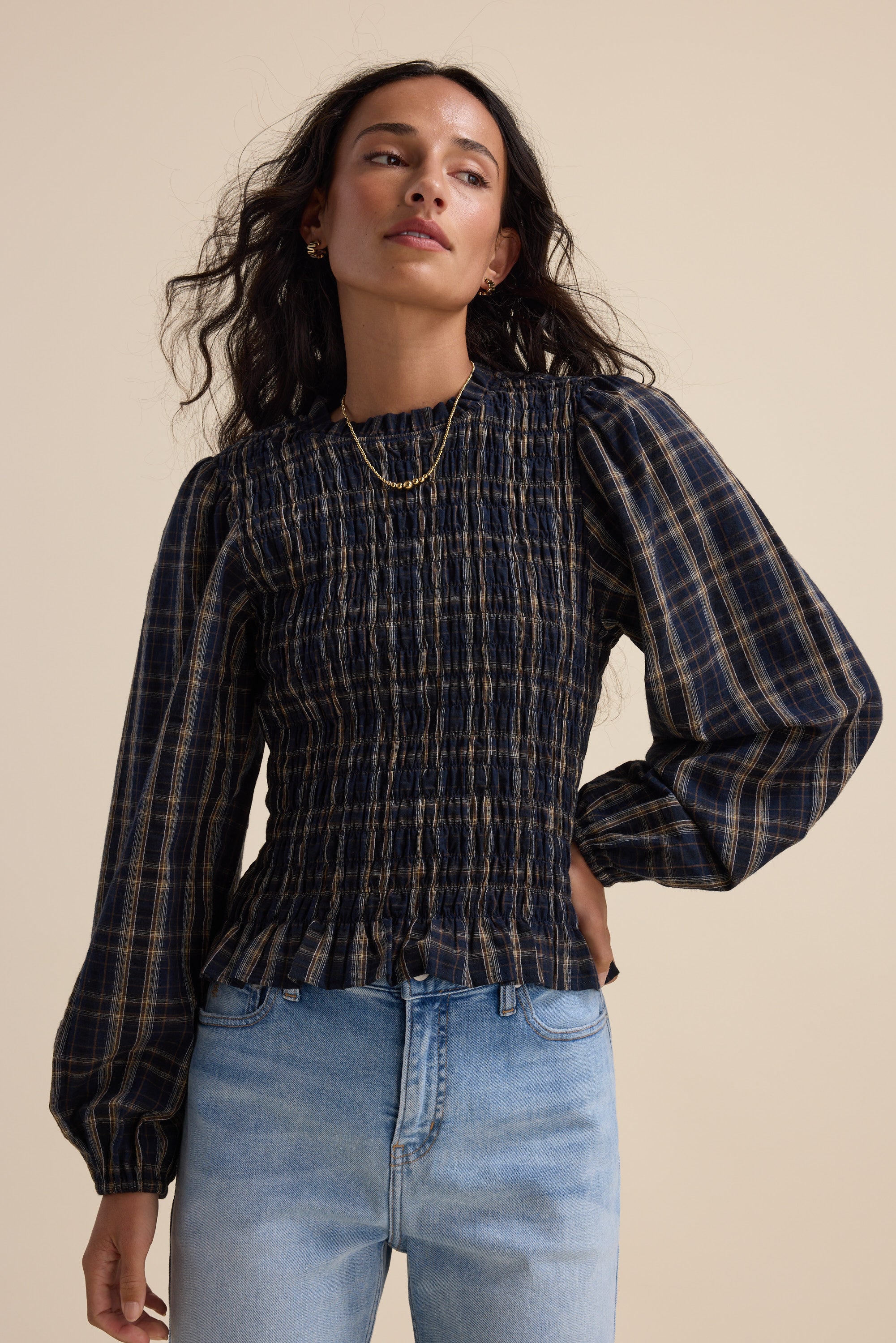 Woman in Elementary Shirred Long Sleeve Top and light blue jeans against a beige background.