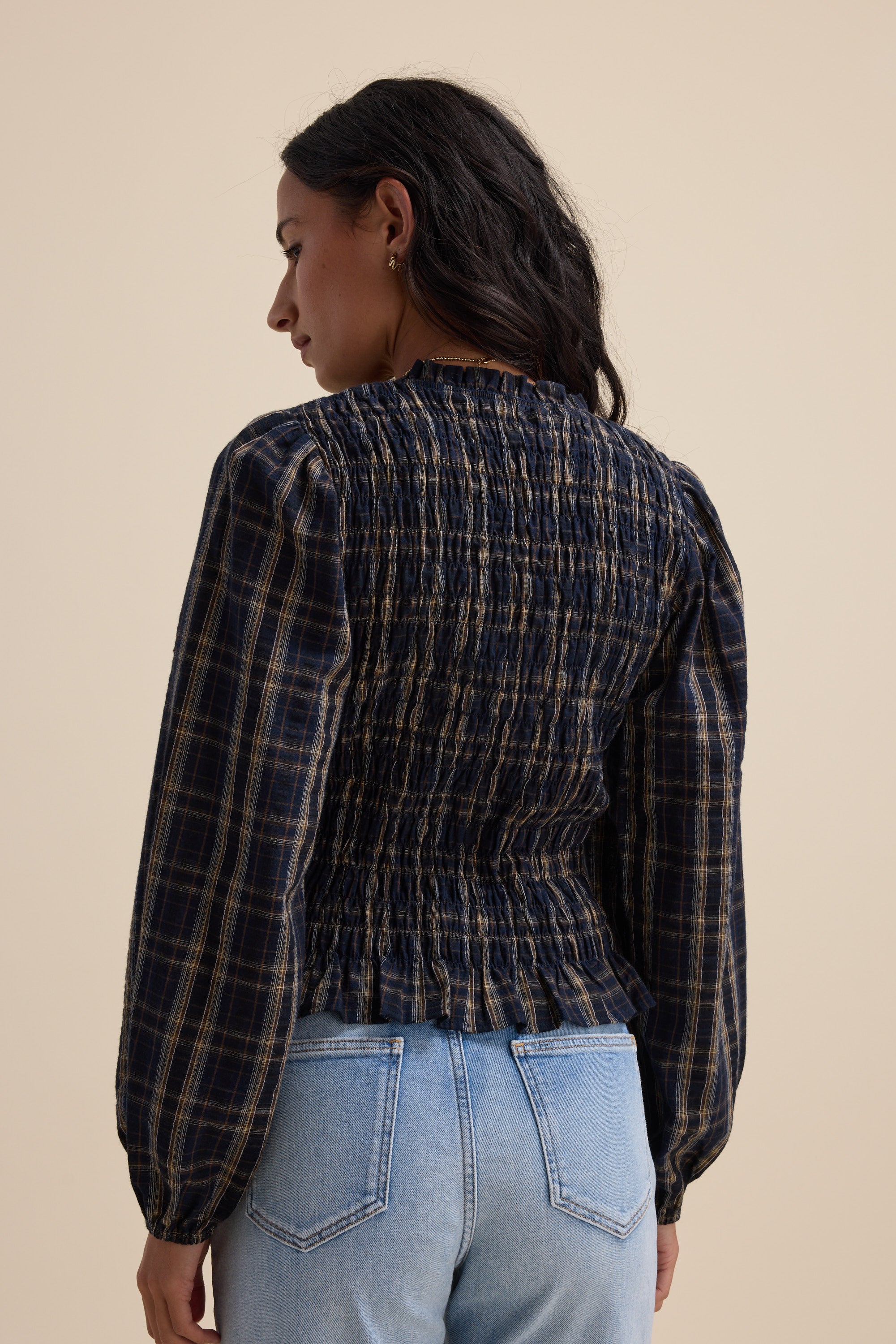 Woman in an Elementary navy check shirred long sleeve top and light blue jeans, back view.