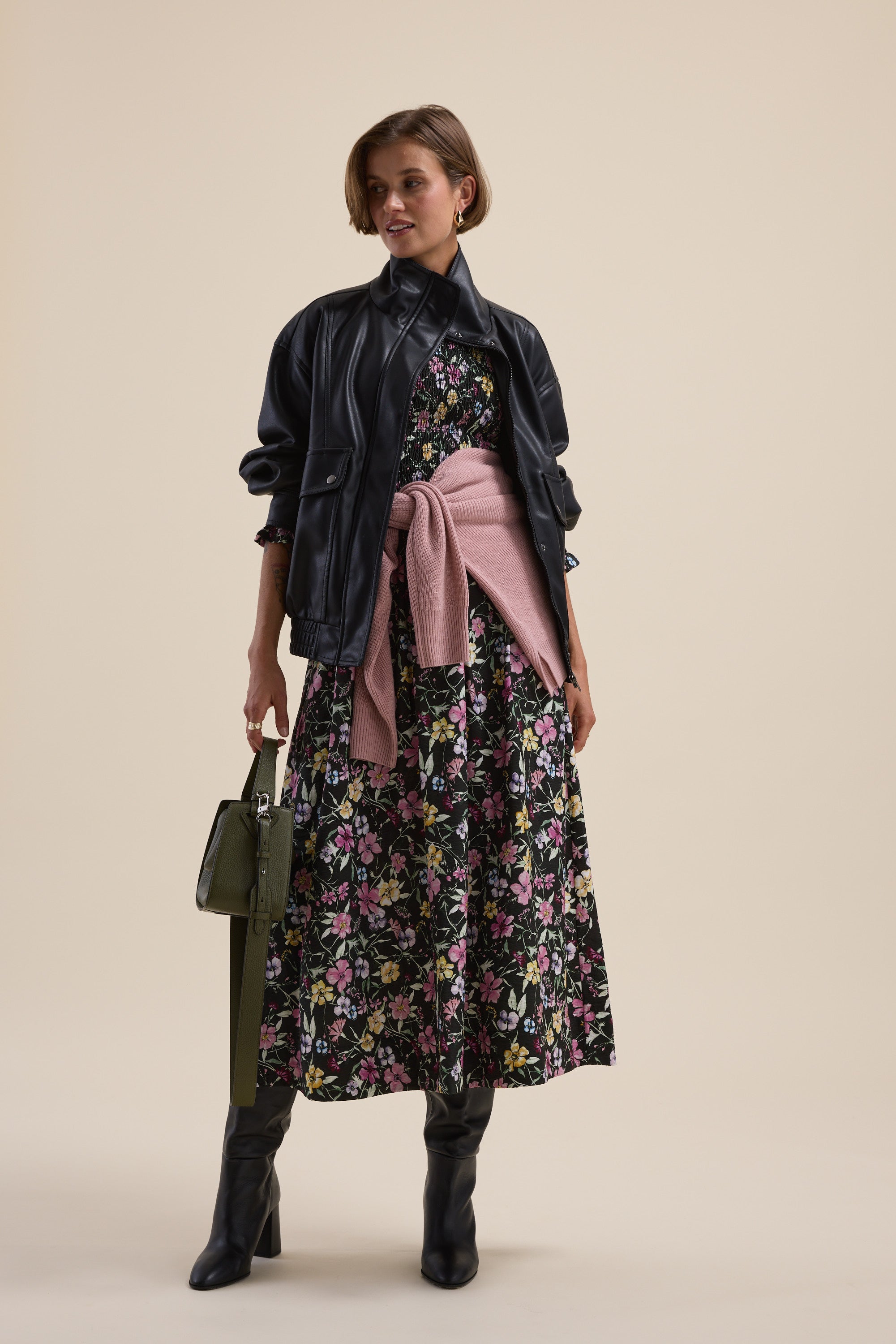 Woman in Max Brooke Shirred Long Sleeve Dress, black jacket, pink sweater, olive handbag.