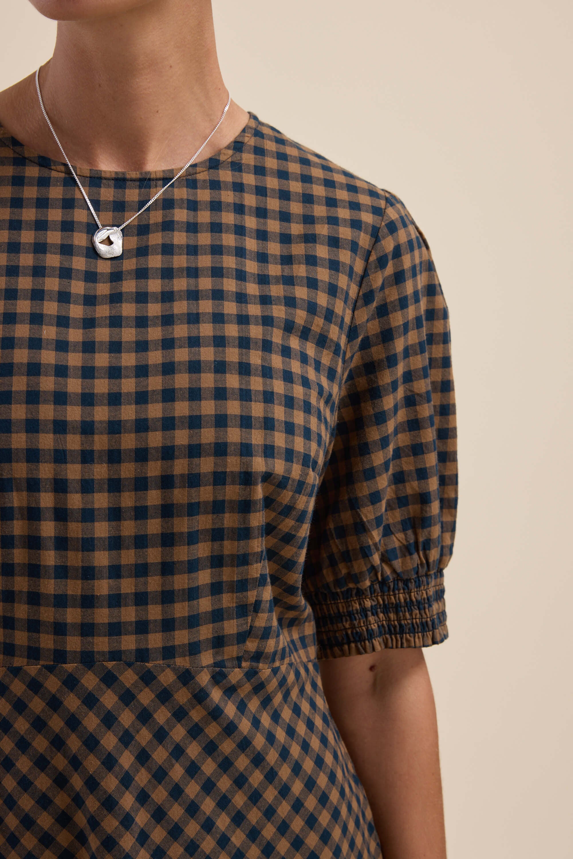 Person wearing the Max Lucy Bias Cut Dress in brown/navy with short sleeves and a silver necklace.