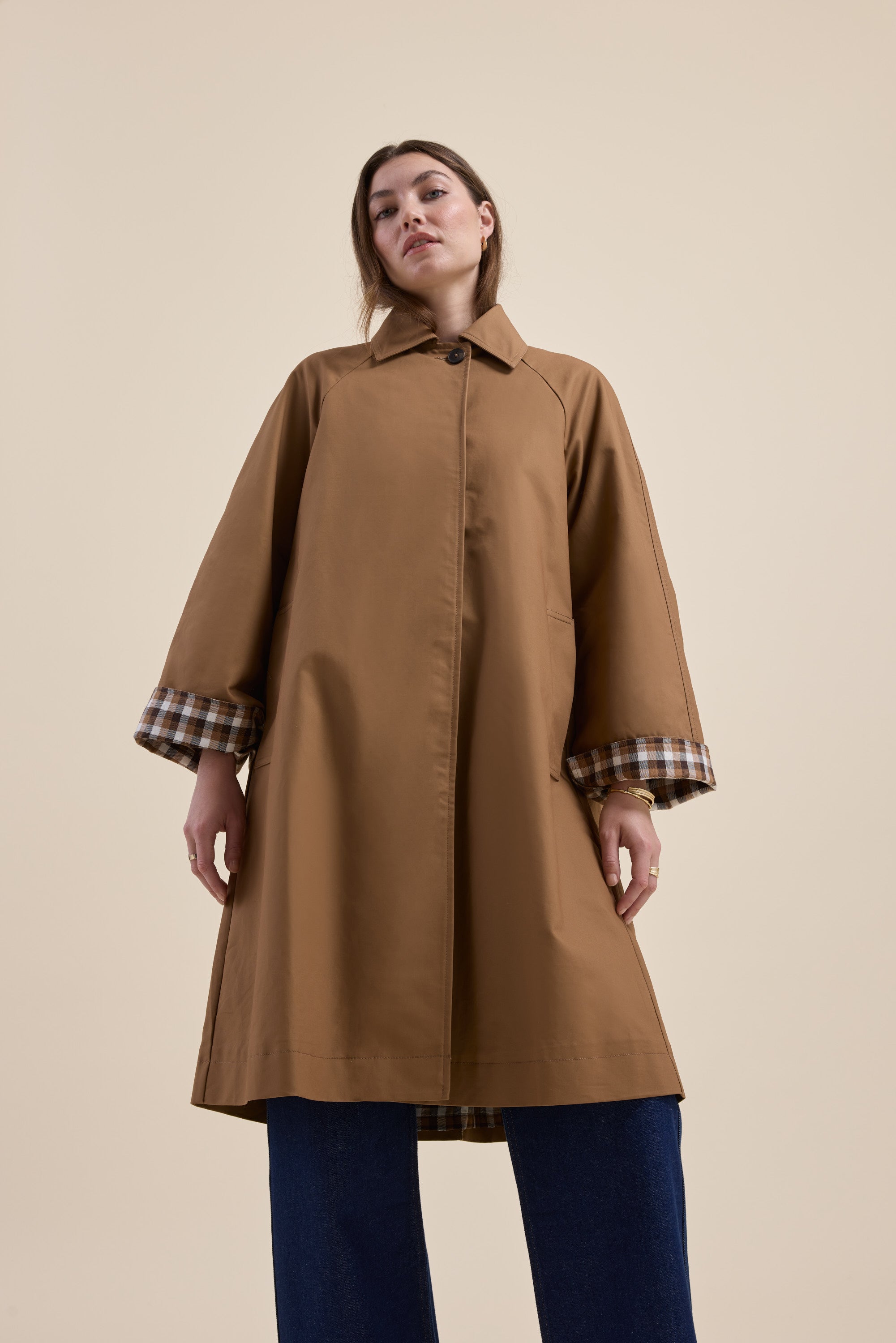 Woman wears Max London Trench Coat with plaid cuffs and blue pants against a beige background.