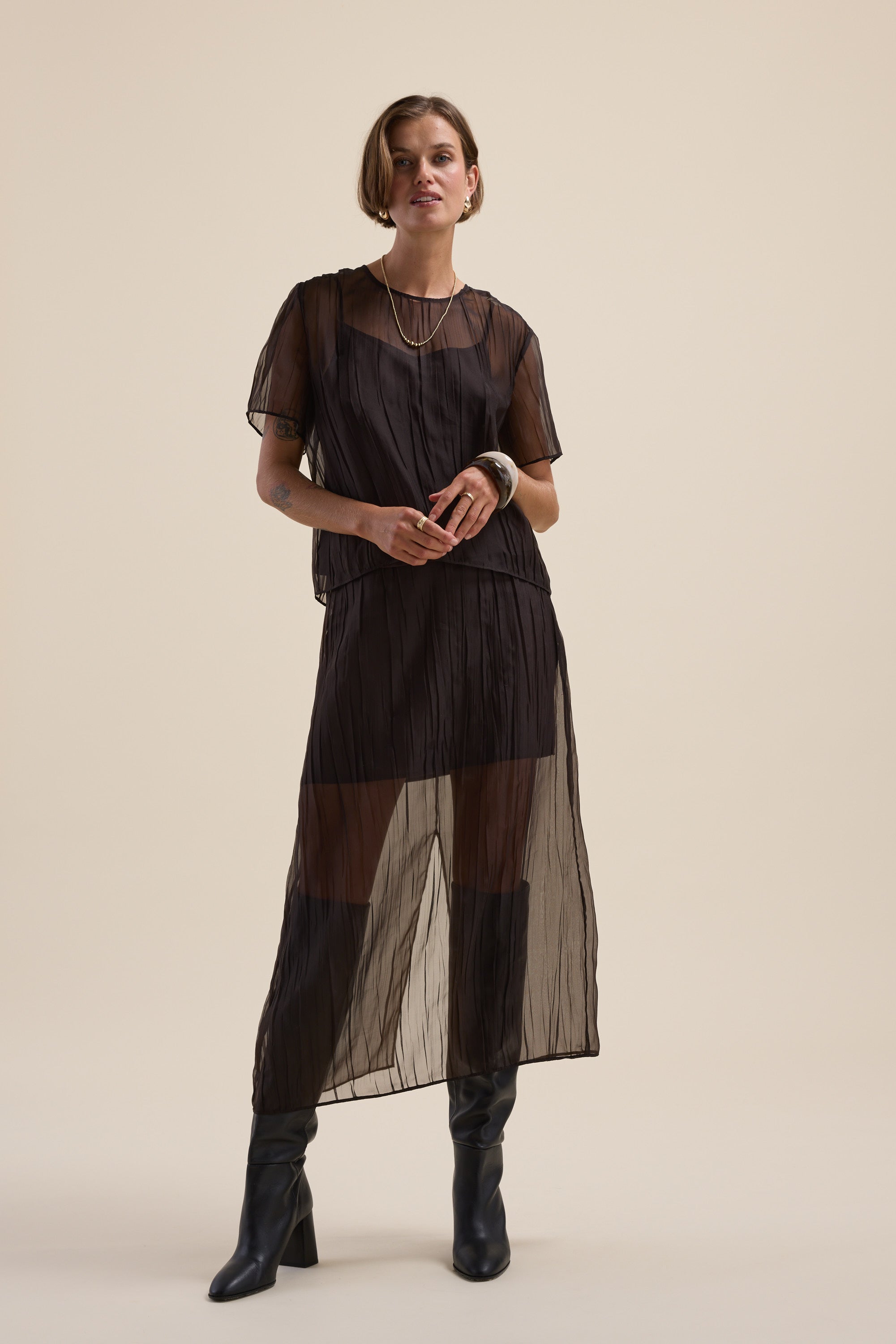Woman in Max's Ari Sheer Midi Skirt over a black slip, with black boots and jewelry.