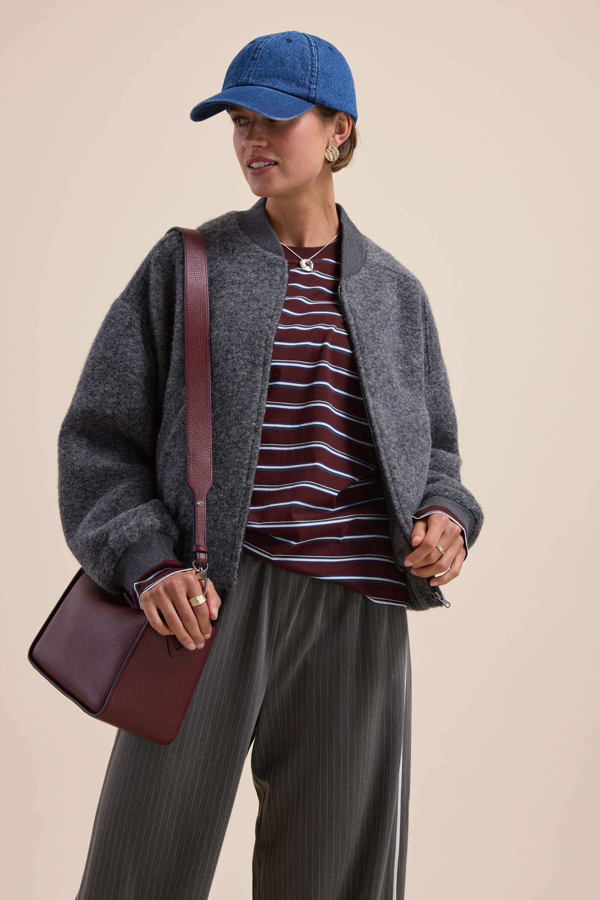 Person in gray jacket, Max Carmen Long Sleeve Stripe Tee, blue cap, pinstriped pants, maroon bag.