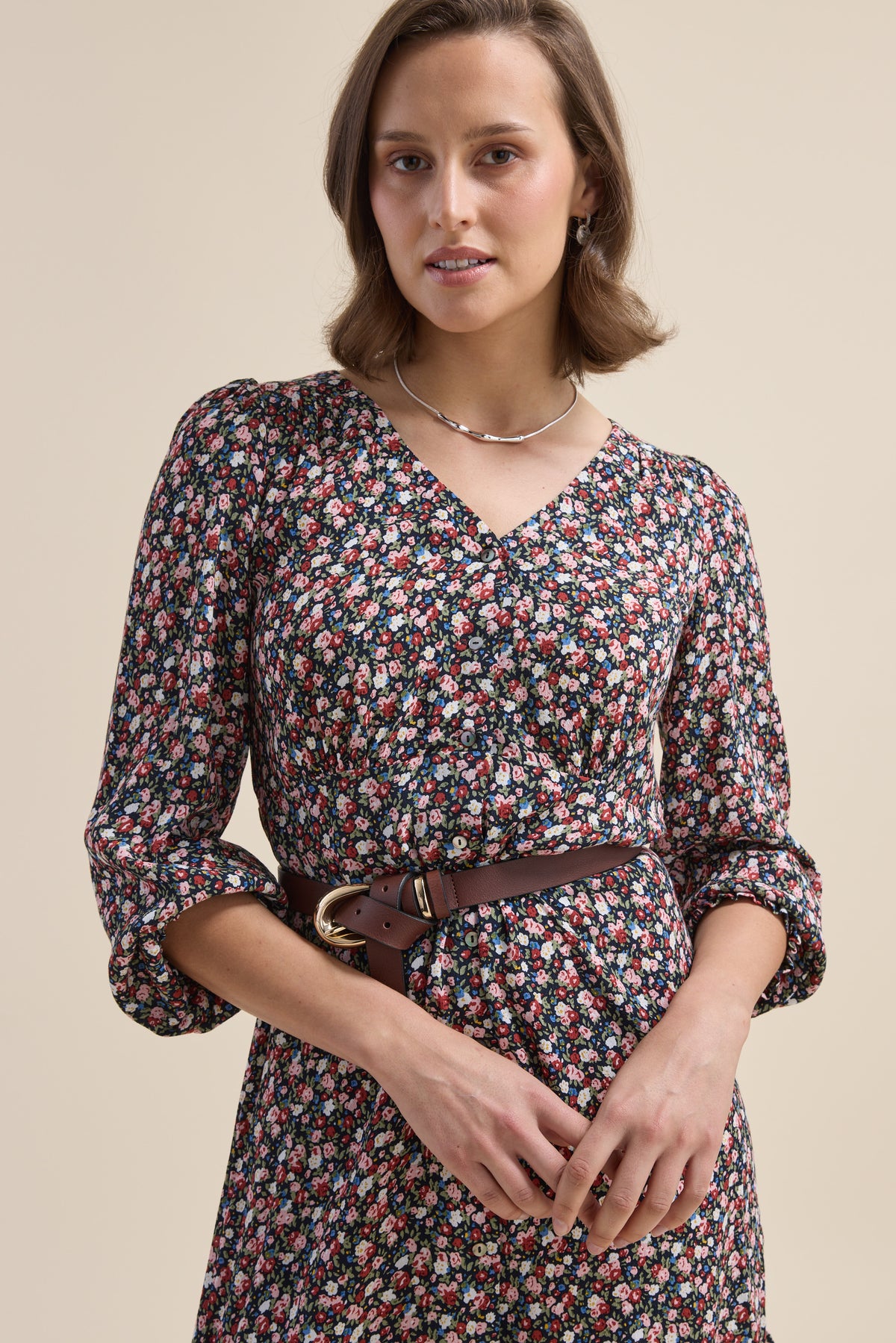 Woman in Elementary Button Front Dress with belt, standing against a plain beige background.
