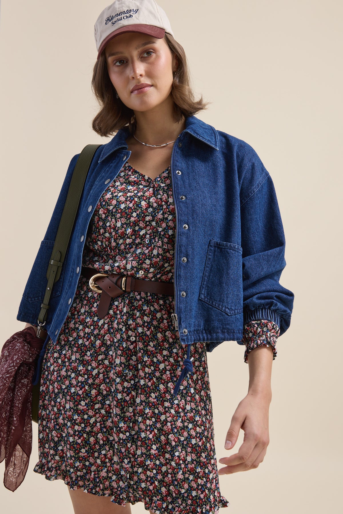 Woman in an Elementary Button Front Dress, denim jacket, cap, belt, and carrying a bag.
