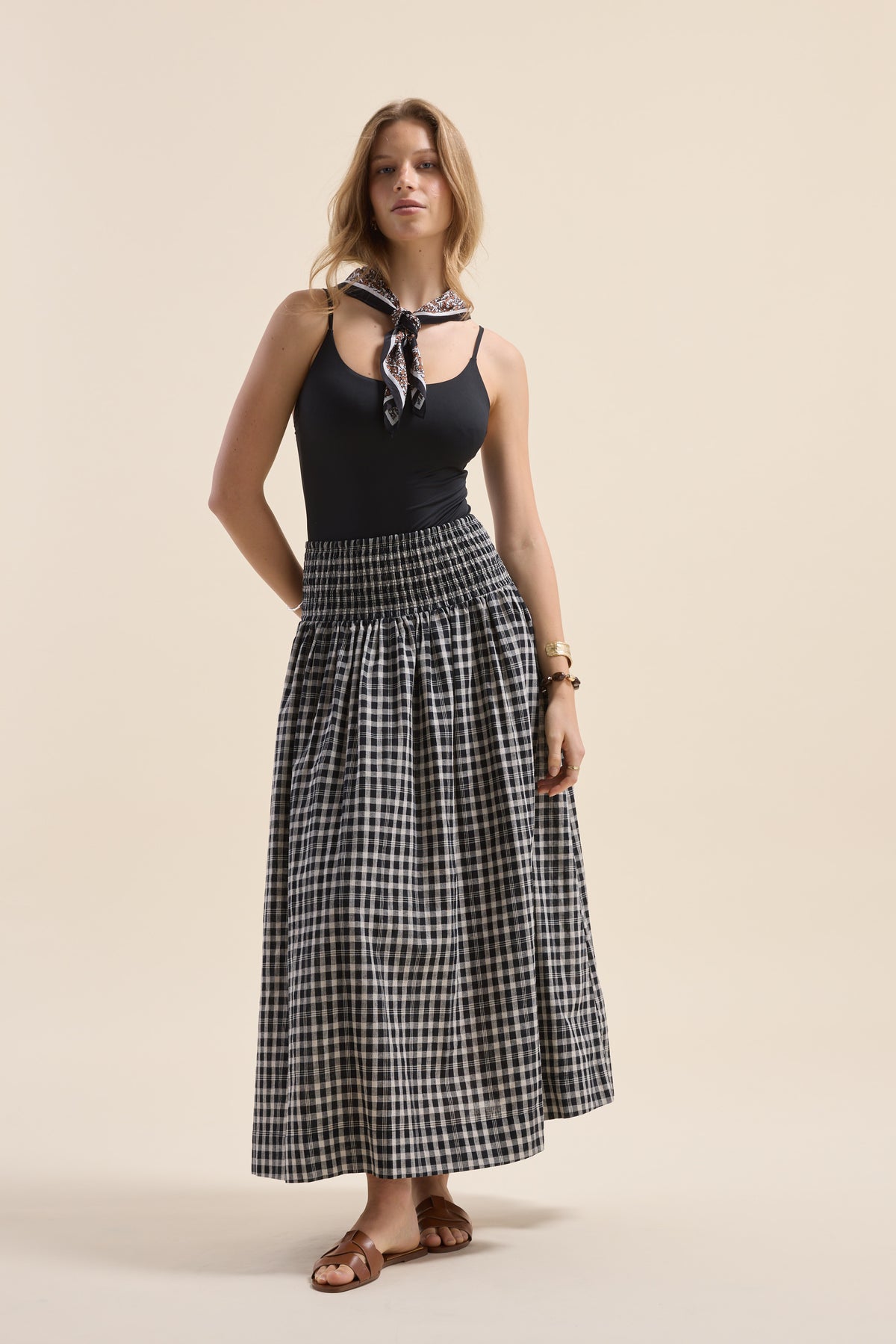 Woman in black tank, Elementary Shirred Drop Waist Skirt, sandals & scarf on beige background.