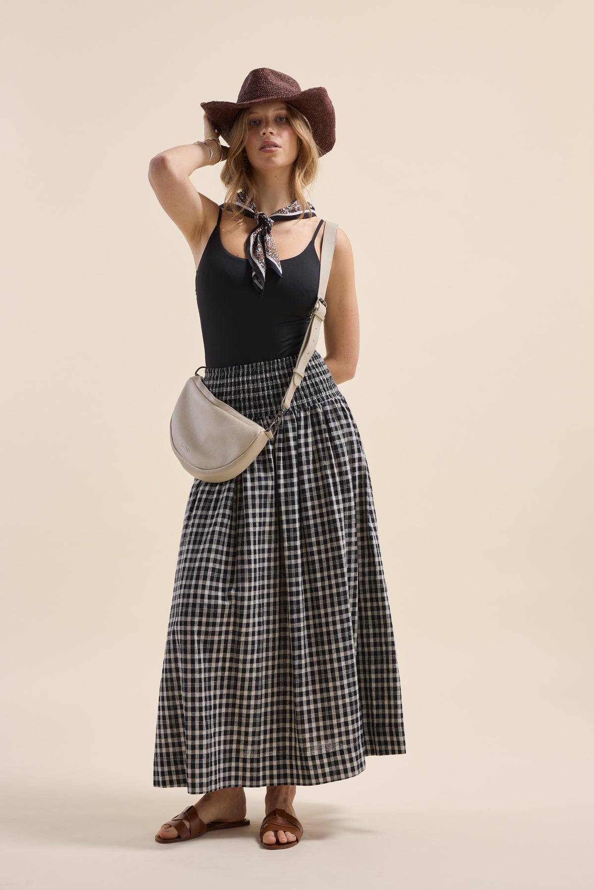 Woman in black tank, Elementary skirt, brown hat, scarf, sandals, and crossbody bag.