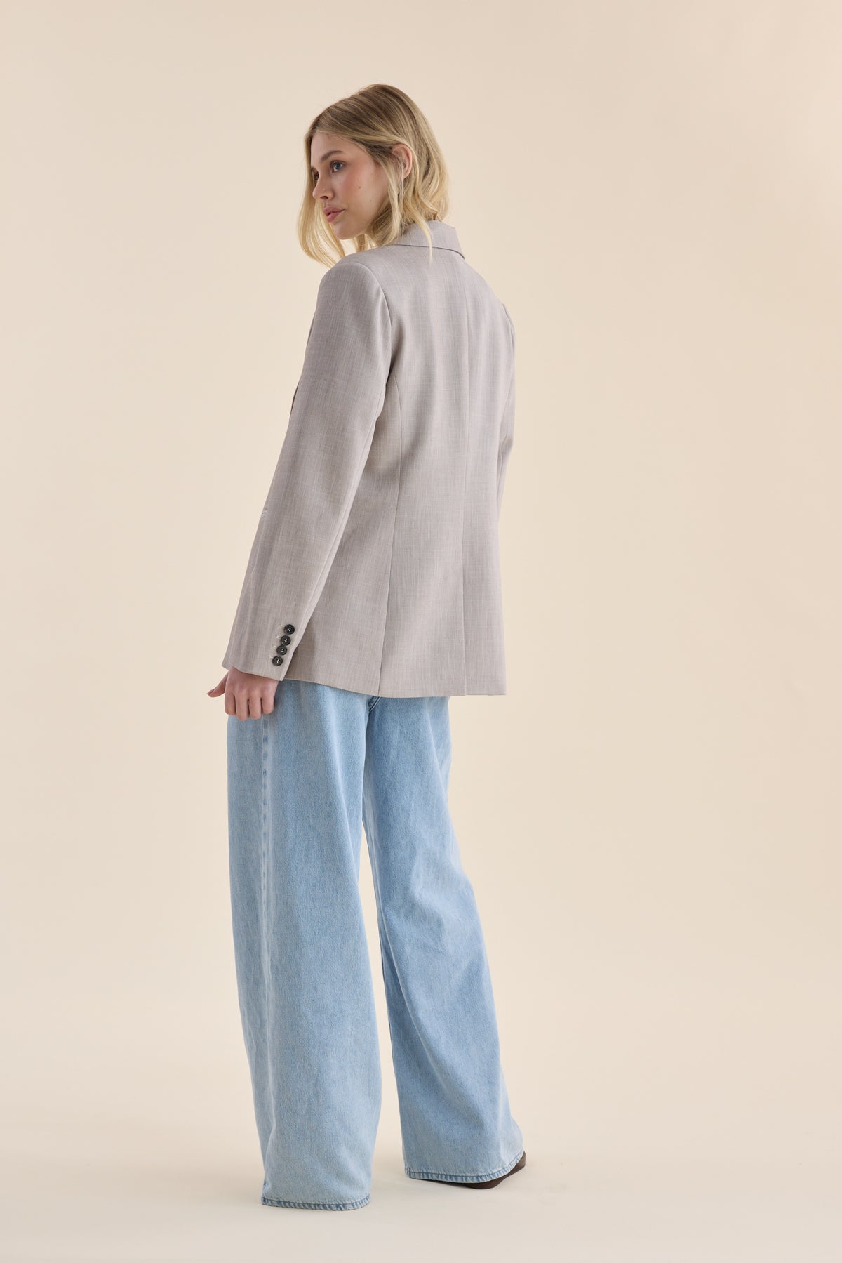 Max The Relaxed Blazer styled with wide-leg jeans, worn by a woman glancing over her shoulder.