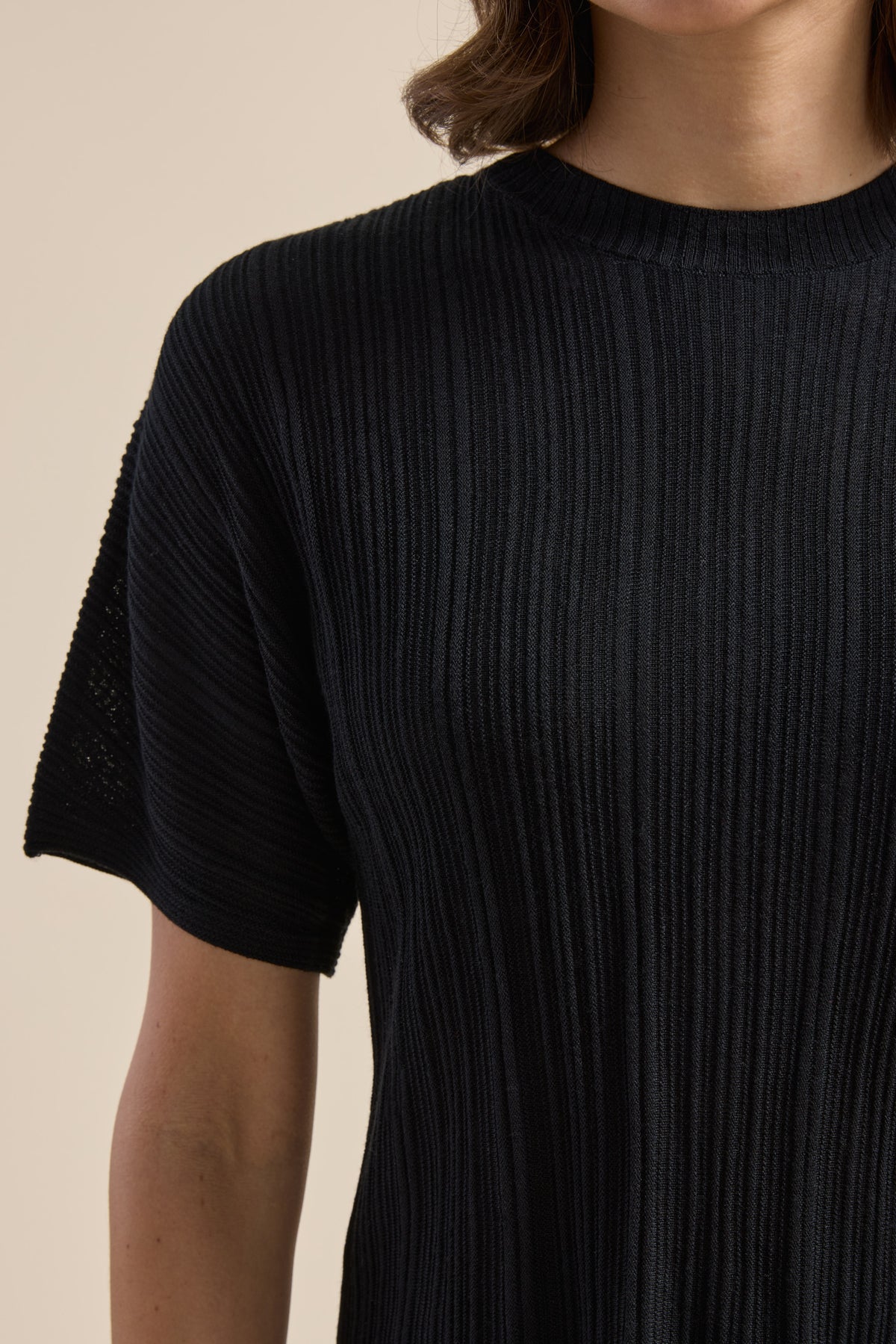 Model in Max’s The Merino Silk Knit Detail Tee, black; shown neck to mid-arm.