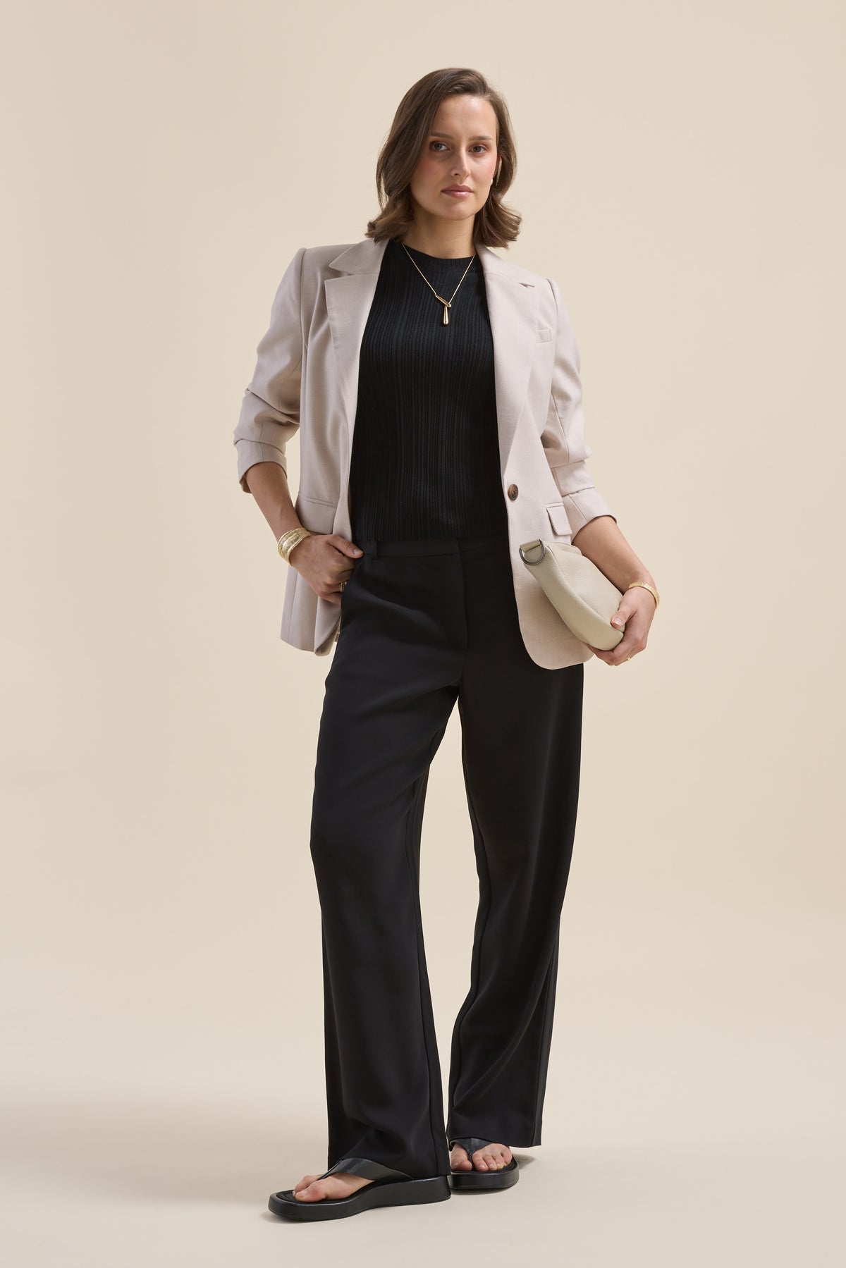 Confident woman in Max’s Merino Silk Knit Detail Tee, beige blazer, black pants, with clutch.