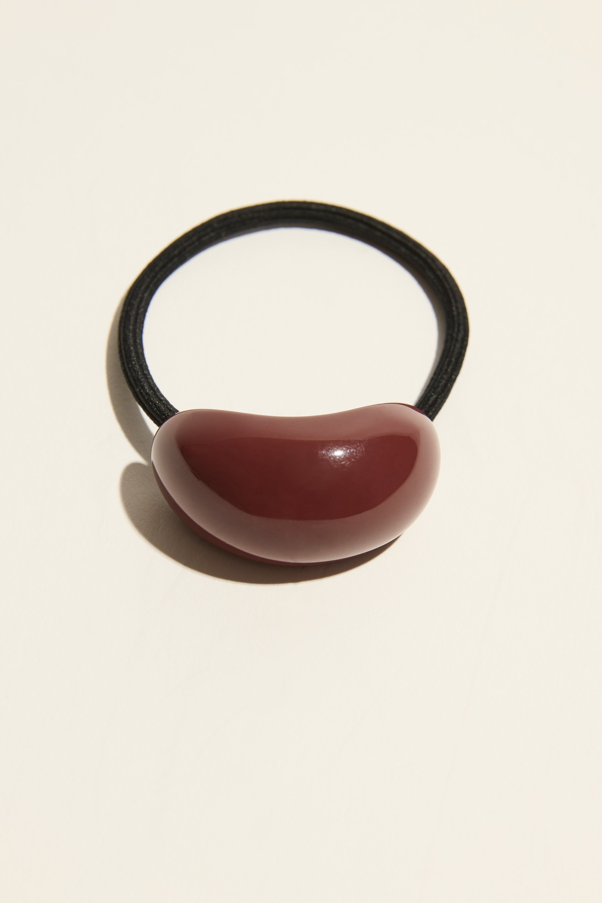 The Janey Resin Hair Tie by Max features a glossy dark red bean accent for polished style.