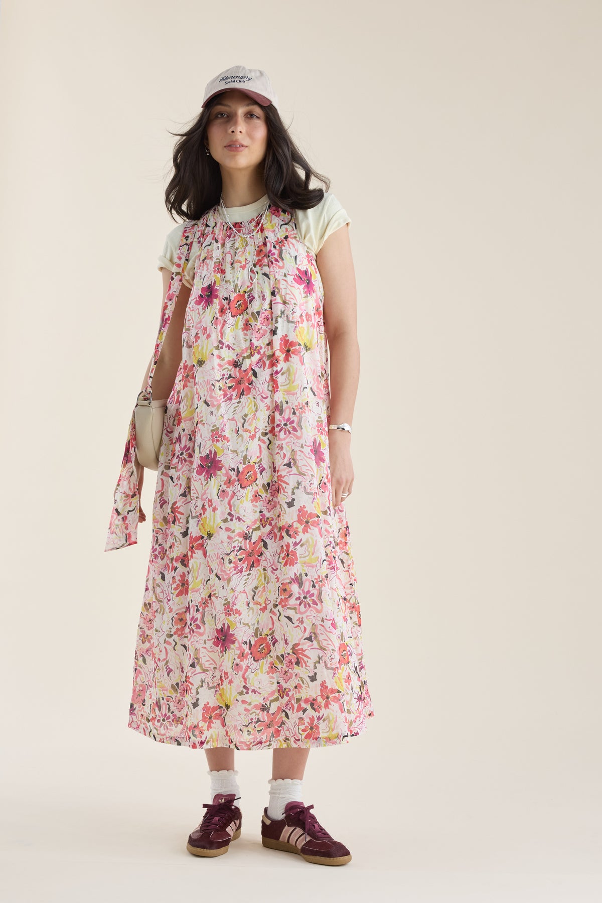 Woman in a Max Kira Back Detail Dress, sneakers, and pink cap stands against a plain background.