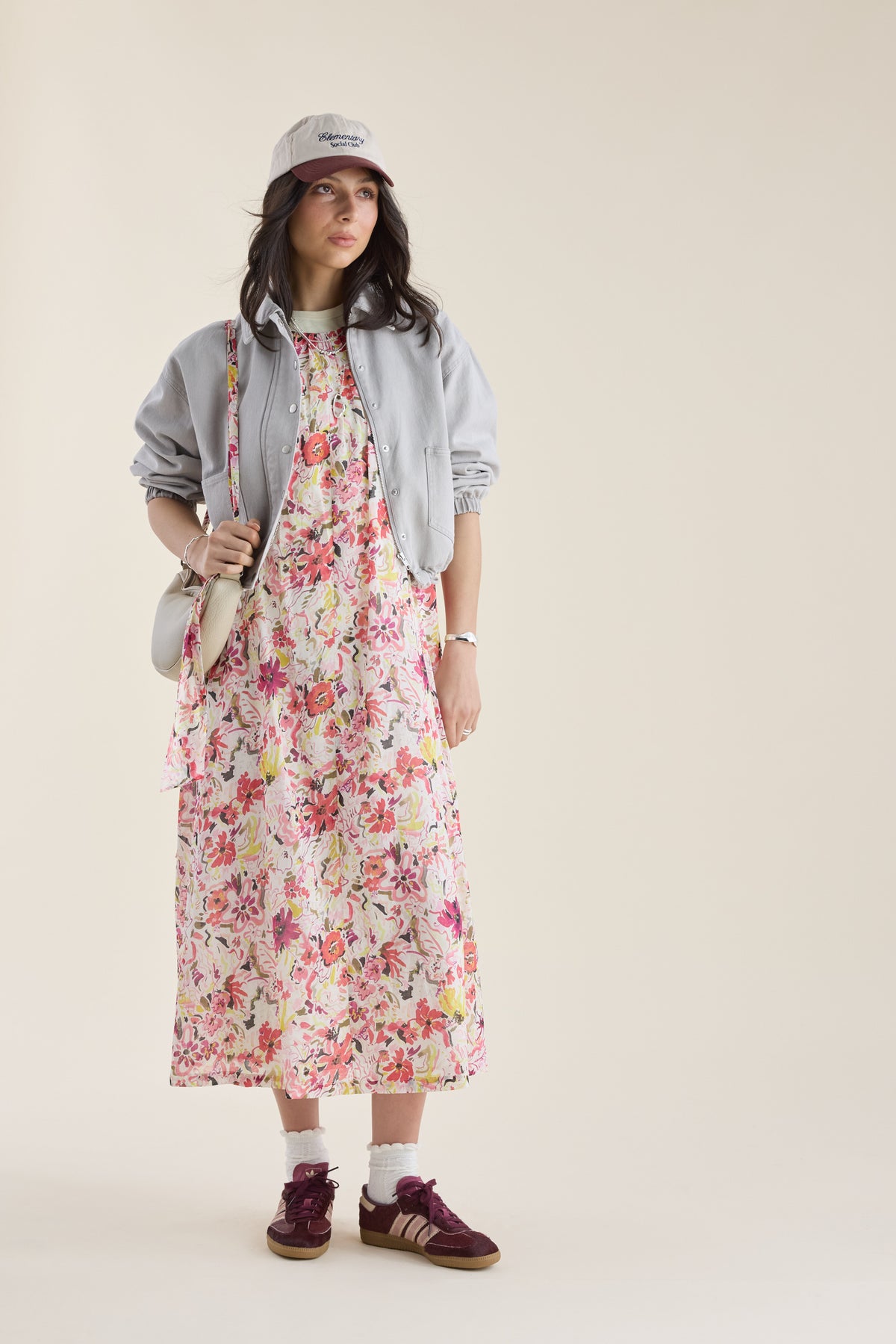 Woman in a Kira Back Detail Dress by Max, gray jacket, cap, sneakers, with a small bag.