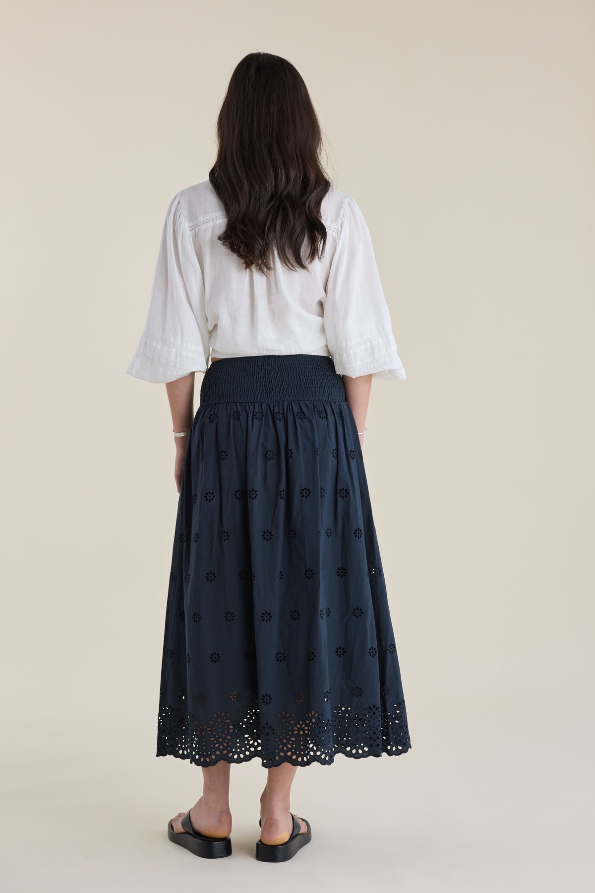 Woman in white blouse and Elementary Broderie Detail Skirt by Elementary, facing away.