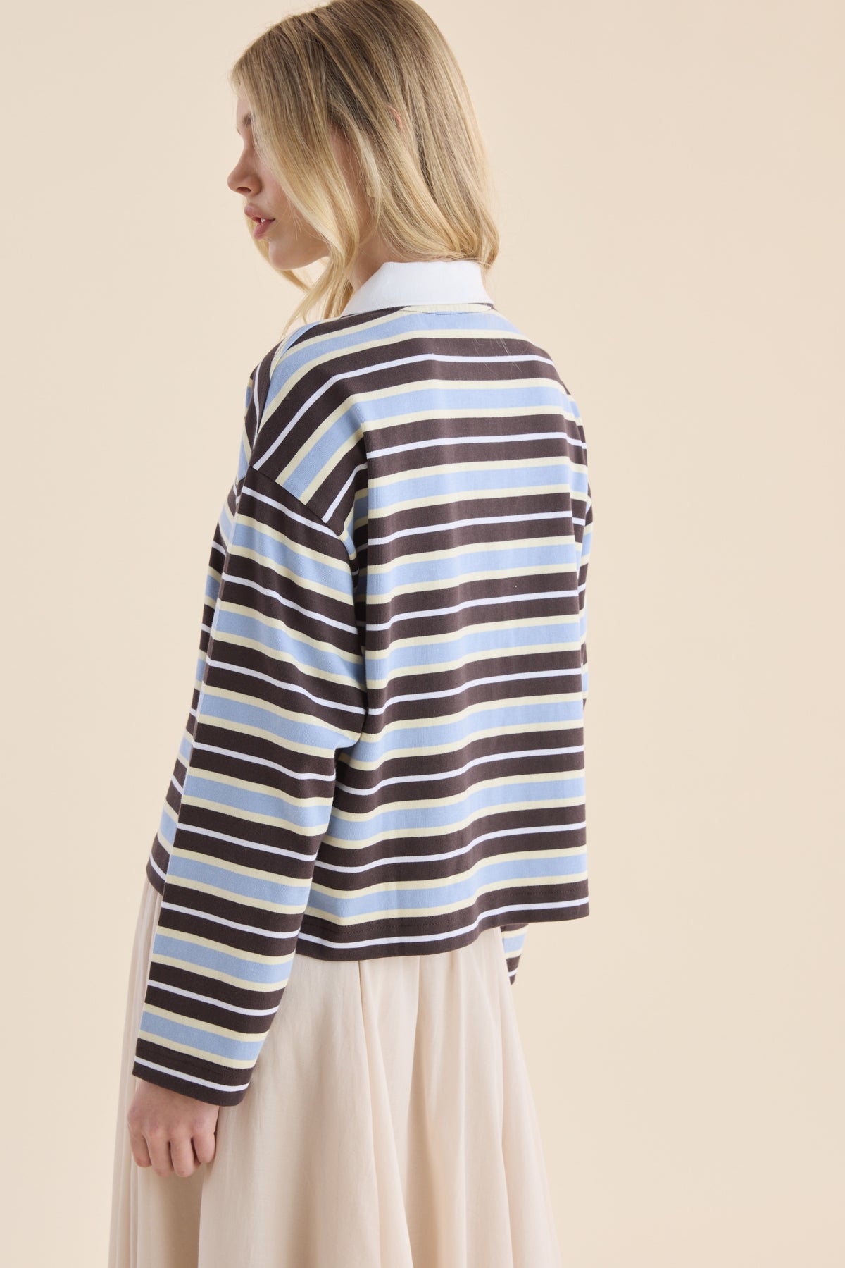 Woman in Elementary Ice Blue Stripe Polo Top and beige skirt, back turned to the camera.