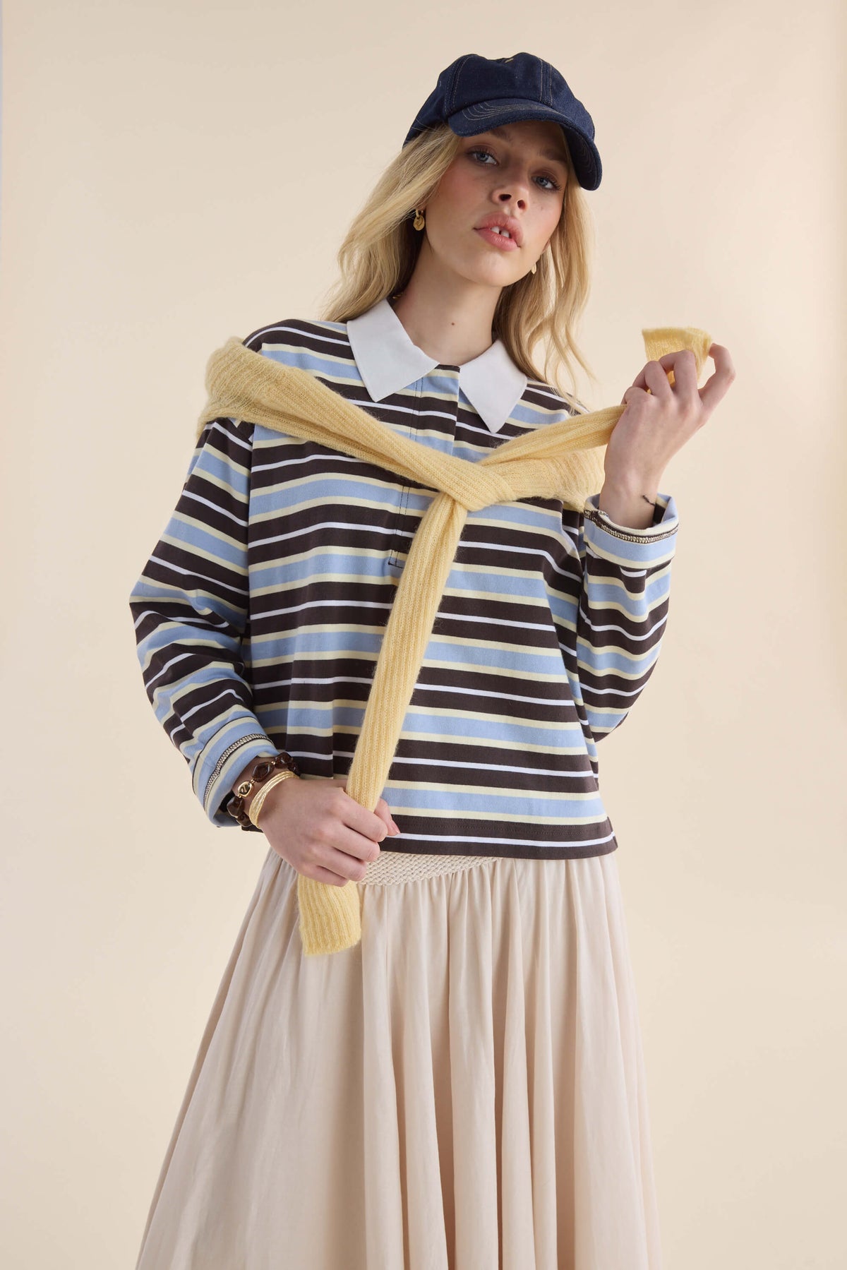 Woman in Elementary Polo Top, cream skirt, yellow sweater draped over shoulders.