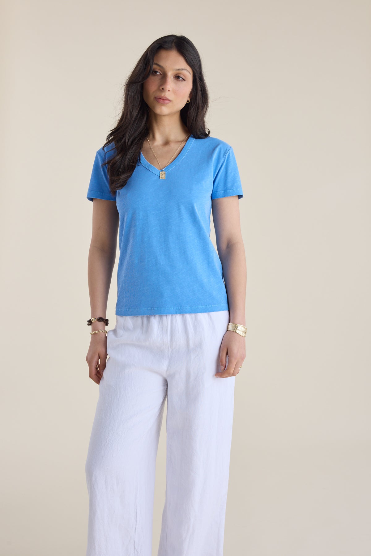 Woman in Elementary Organic Cotton Slub V Neck Tee and white pants, beige background.