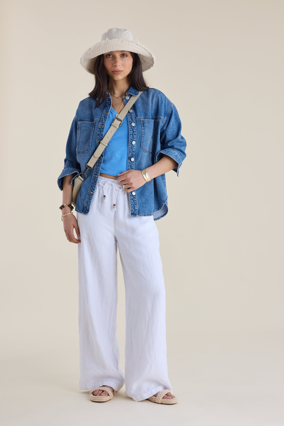 Woman in denim shirt, white pants, sun hat, Elementary blue V-neck tee, sandals, facing forward.