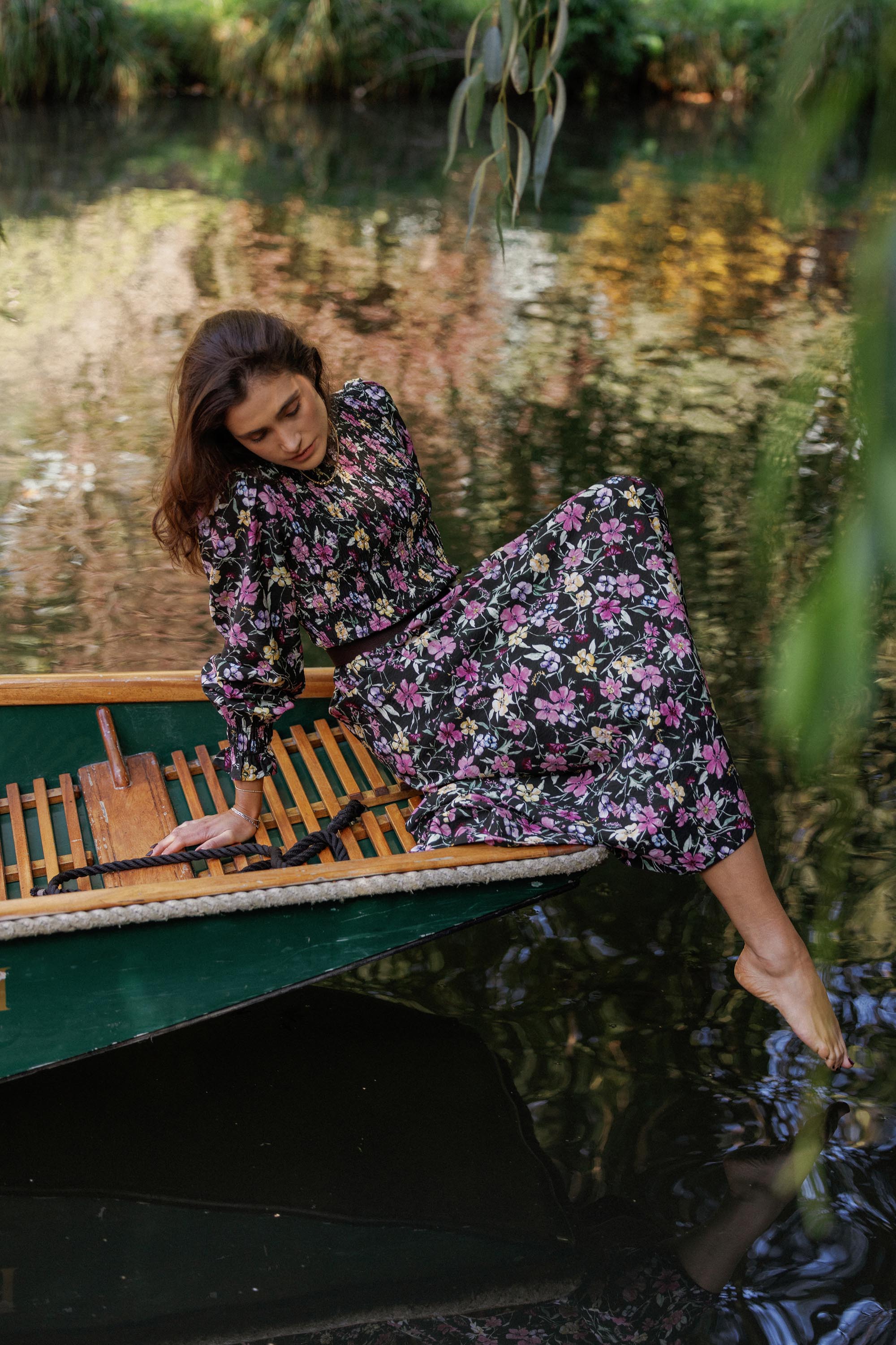 Woman in the Max Brooke Shirred Long Sleeve Dress sits on a boat, touching the water.