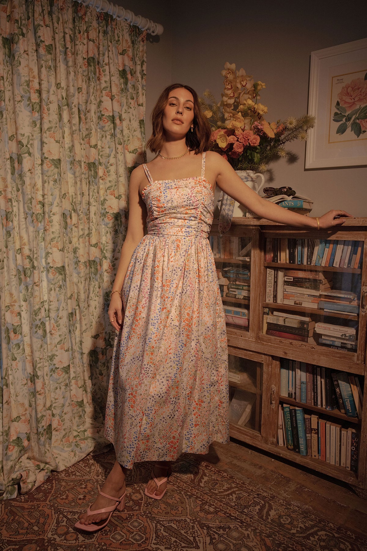 A woman standing in a house wearing a floral dress.