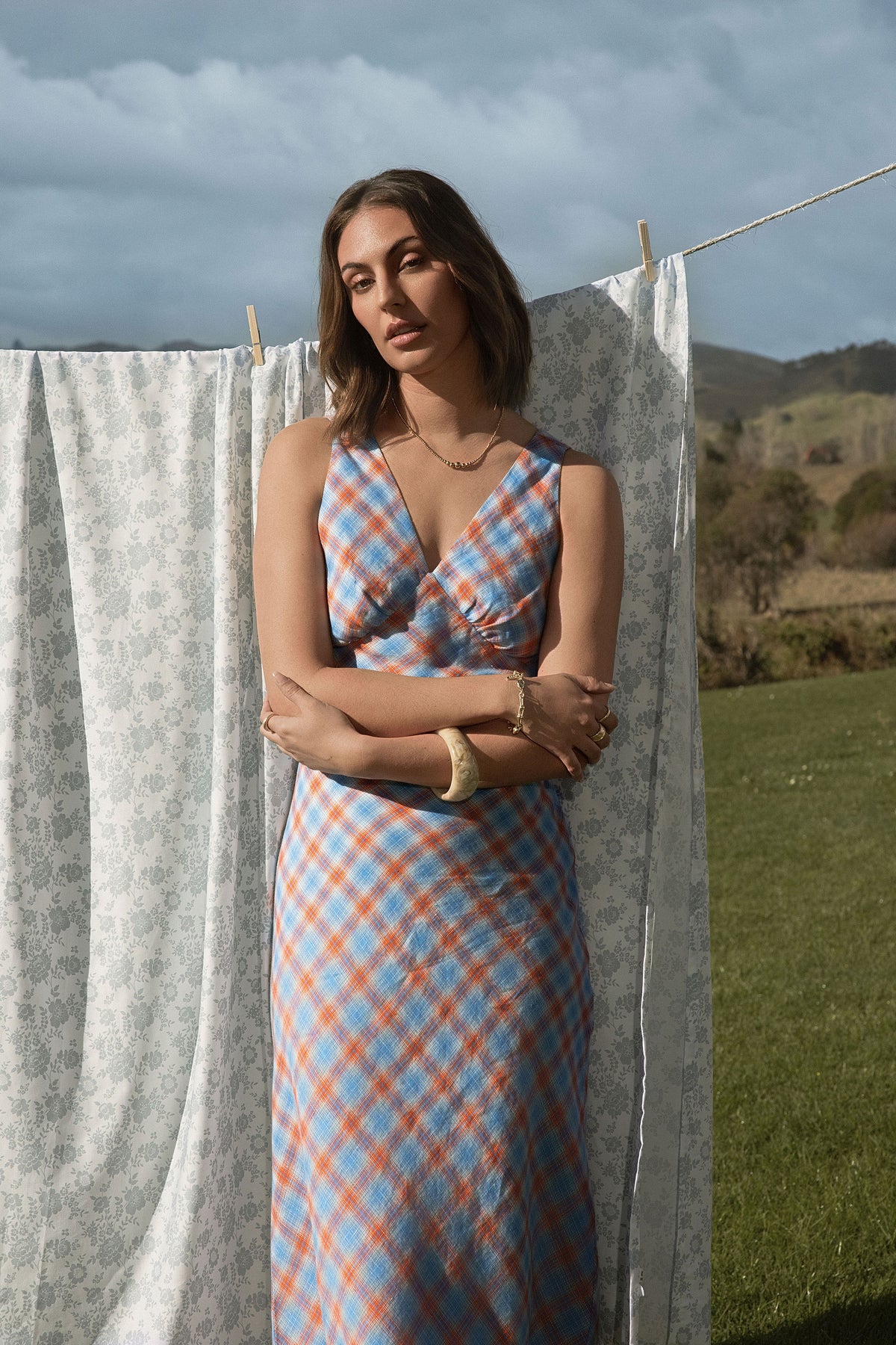 A woman standing in front of a washing line wearing a blue checkered dress.