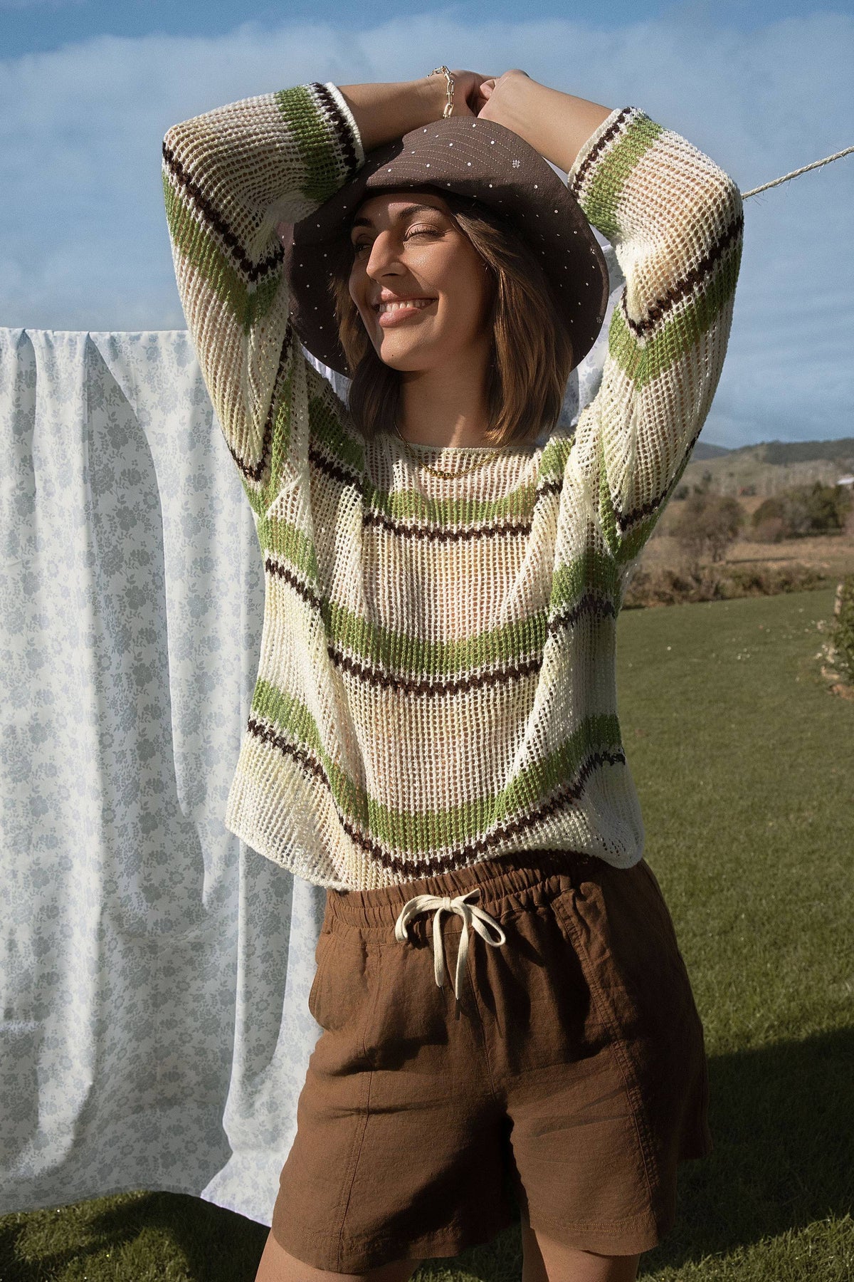 Woman enjoys a sunny day by the laundry line in the Elementary Linen Mesh Knit Sweater.