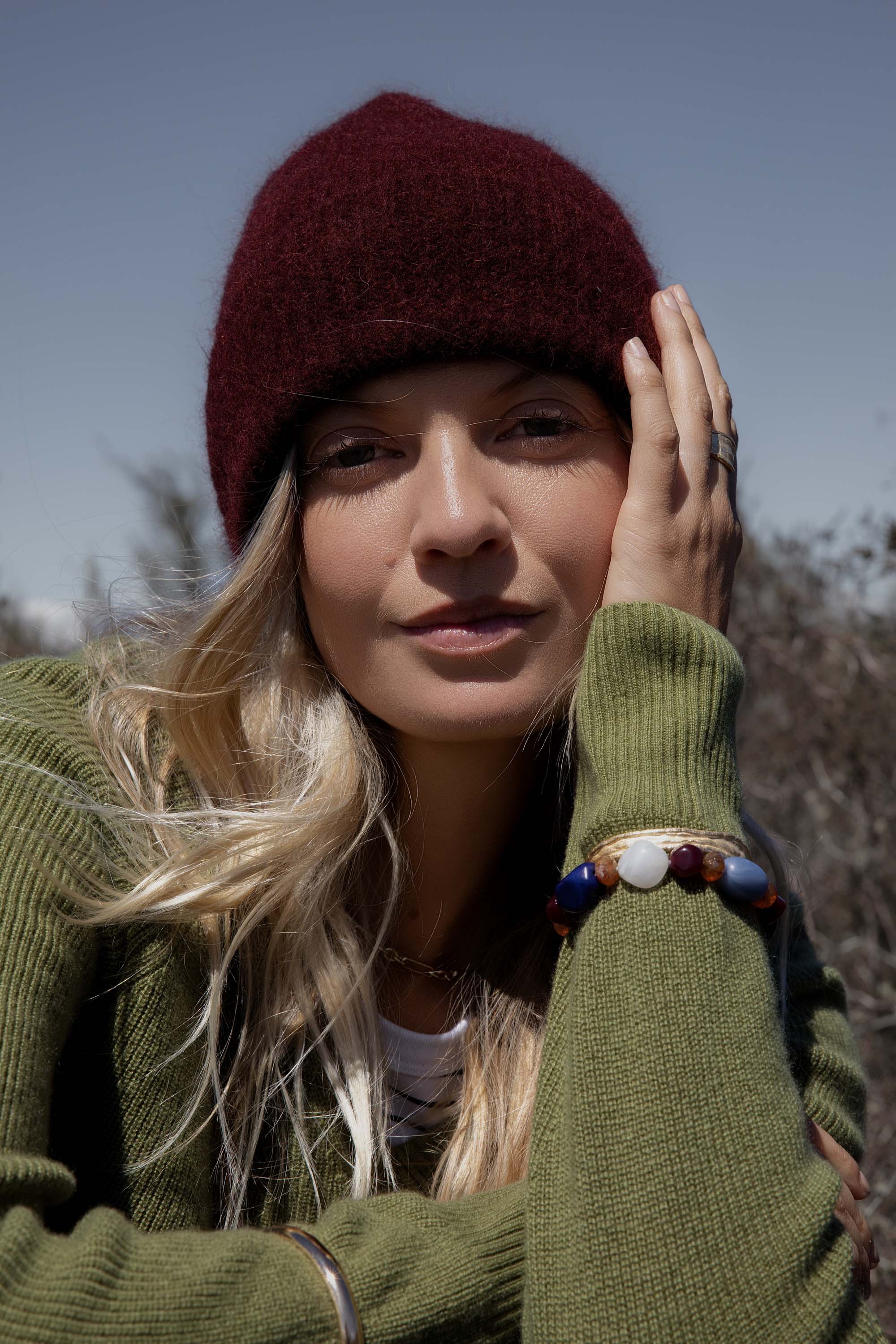 Woman in a Georgia Luxe Whisper Knit Beanie by Max and green sweater, relaxing outdoors.