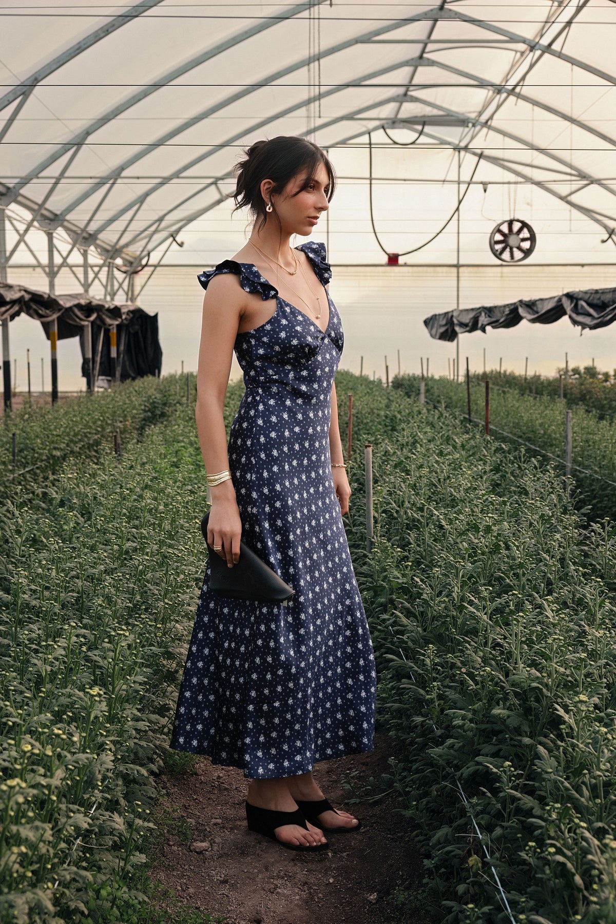 A woman standing in a greenhouse wearing a blue floral dress.