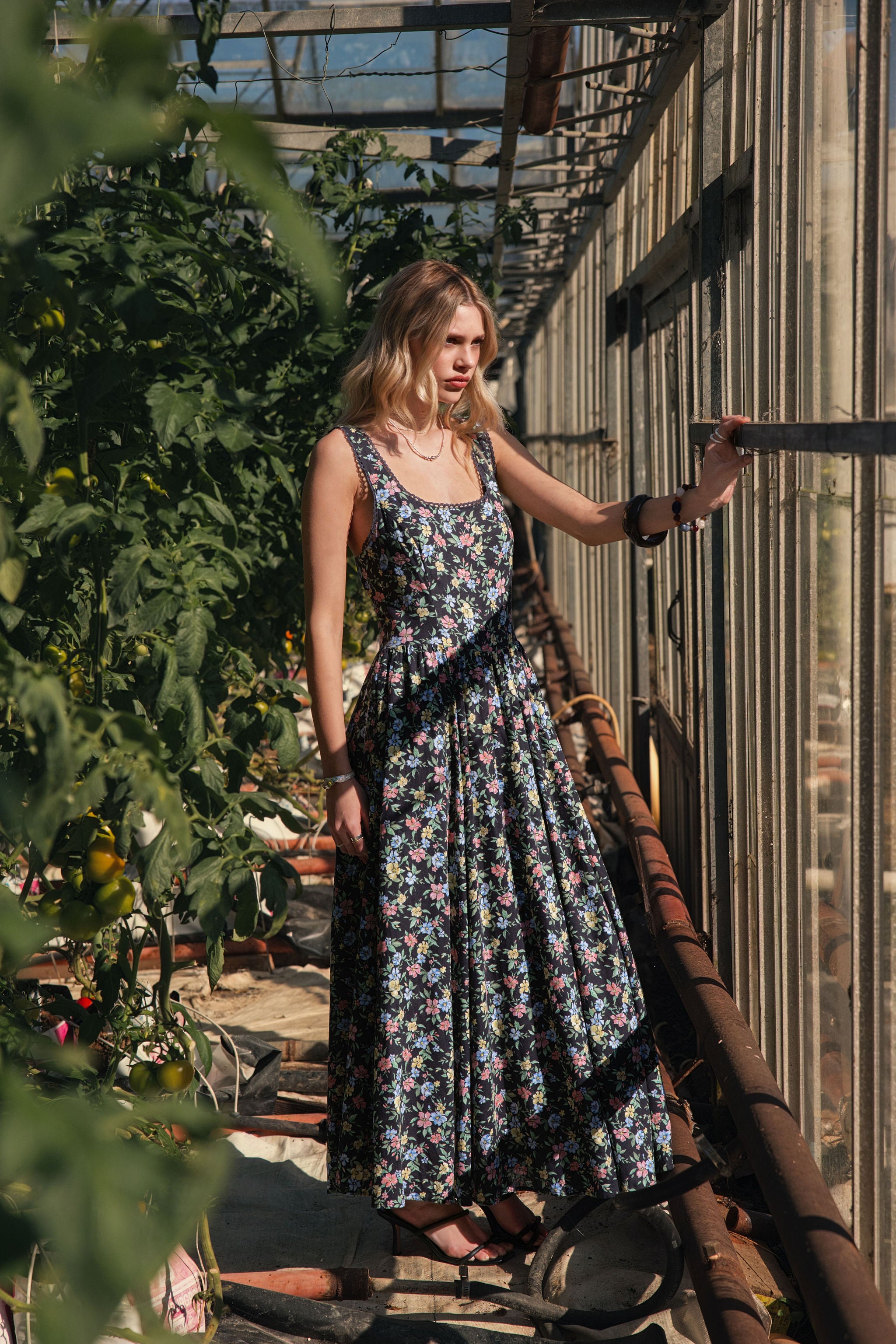 A woman standing in a greenhouse wearing a floral spring midi dress.