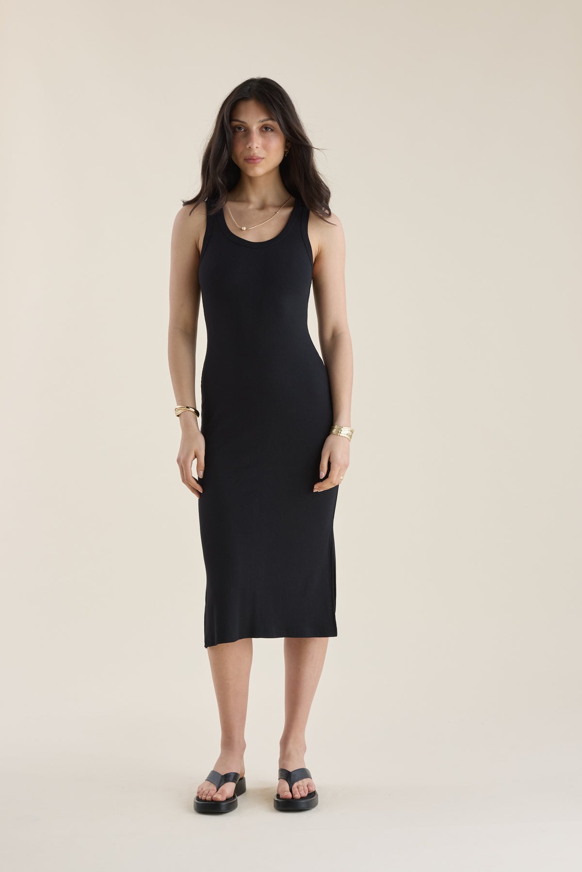 Woman wears the Elementary Basics Tank Slip Dress in black, posing against a beige background.
