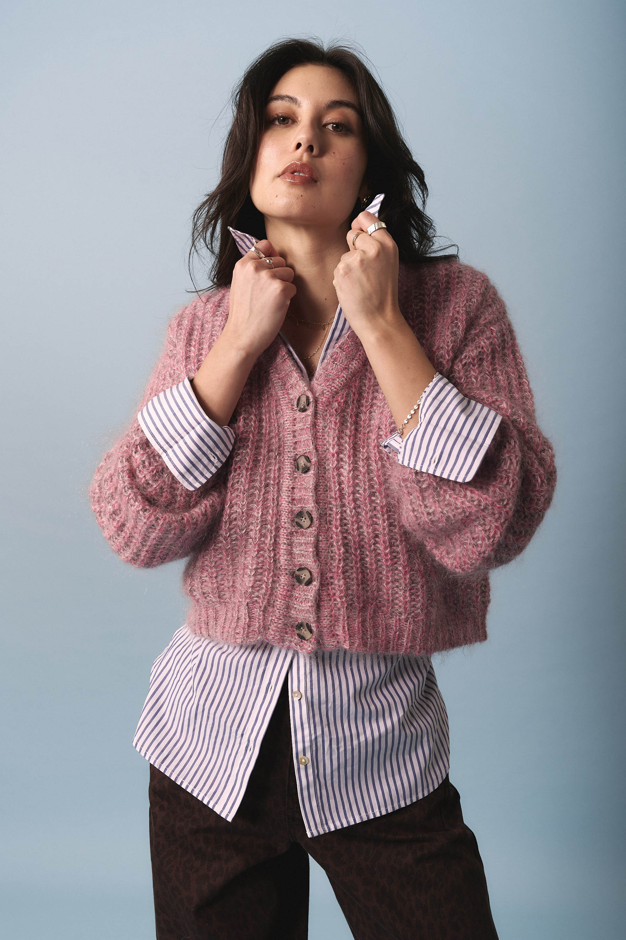 A woman poses against a light blue background, confidently modeling the Max Lennox Whisper Knit Cardigan over a blue and white striped shirt and dark patterned pants.